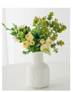 Close-up detailed view of artificial yellow rose bouquet with eucalyptus in a minimalist white vase