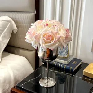 Eleganter kleiner künstlicher Rosenstrauß in einer silbernen Kelchvase auf dem Nachttisch