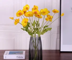 Ramo de amapolas artificiales amarillas en un jarrón de cristal gris para el hogar