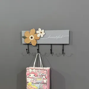 Close-up detail of a minimalist wooden wall coat rack with four black hooks and flower decor