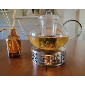 Stainless steel tea warmer base with decorative hollow pattern holding a glass teapot