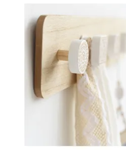 Detailopname van houten wandkapstok met gesneden witte decoratieve haken in boho-stijl