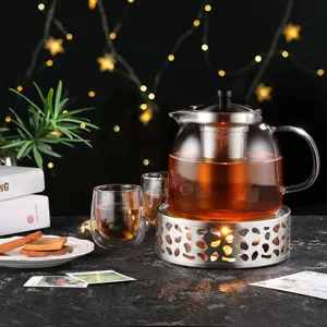 Stainless steel teapot warmer base with glass tea pot in cozy evening setting