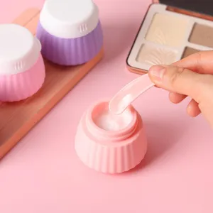 Macro detail of portable pink silicone cream jar showing white lotion texture and scoop