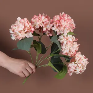 Detailopname van hand die een roze kunstmatige hortensiaboeket met 5 koppen vasthoudt.