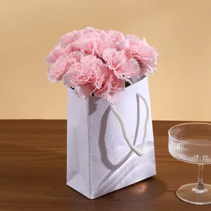 Belles oeillets artificiels roses présentés dans un sac cadeau blanc texturé pour la maison