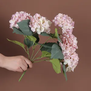 Hand die een kunstmatig hortensiaboeket met vijf roze en crème bloemen vasthoudt