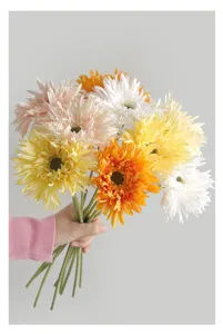 Hand holding a bouquet of colorful artificial brushed Gerbera daisies for home decor.