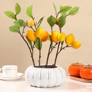Decorative lifelike artificial lemon branches with green leaves in a white ceramic vase
