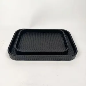 Detailed view of two nested black woven leather storage trays with elegant Intrecciato texture.