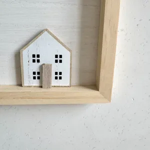 Detailed view of a small white wooden house ornament within a minimalist Nordic frame.