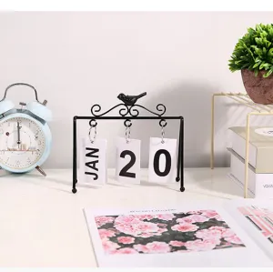 Detailed macro view of a Nordic style black iron bird flip calendar on a minimalist desk
