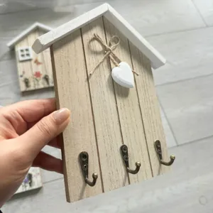 Close-up of house-shaped wooden key holder with heart charm and three bronze metal hooks.