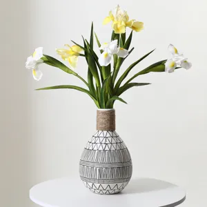 Detailed view of artificial yellow and white iris flowers in a patterned ceramic vase.