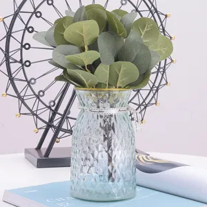 Detailed view of artificial eucalyptus money leaves in a textured clear glass vase with ribbon.