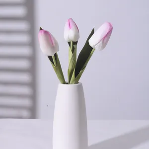 Realistic artificial pink and white tulips in a minimalist white ceramic vase with shadow