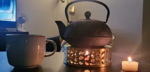 Modern stainless steel teapot warmer base with heart-shaped cutouts in a cozy candlelit setting