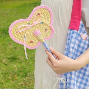 Close-up of a handmade woven heart-shaped straw fan with pink fabric trim and rhinestones