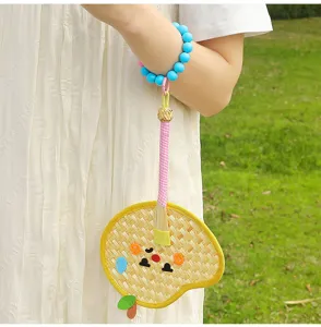 Detailed view of a handmade woven palm leaf fan charm with blue beads and cartoon face