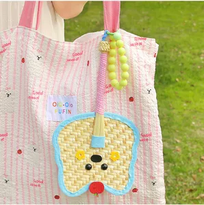 Close-up detail of a cute hand-woven palm leaf fan pendant with a cartoon face on a bag