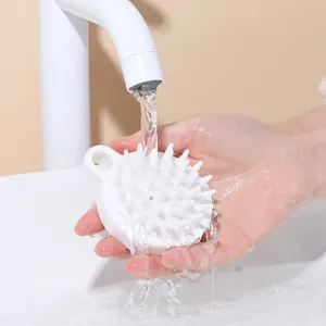 White silicone scalp massager brush being rinsed under running water in a sink.