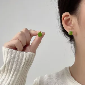 Close-up of a minimalist green square stud earring worn on ear and held by hand