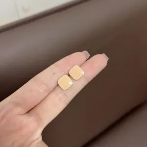 Close-up of minimalist square macaron beige stud earrings held between two fingers