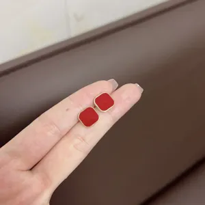 Close-up of retro red square stud earrings with gold trim held on a person's fingers