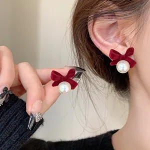 Close-up macro detail of elegant red velvet bow stud earrings with a white pearl
