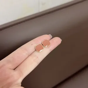 Detailed macro view of minimalist square stud earrings in caramel brown held by fingers