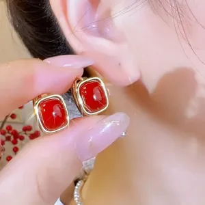 Detail shot of elegant red square stud earrings with golden frame held near an ear.