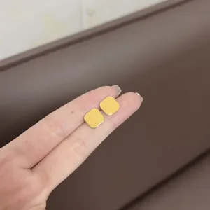 Close-up of simple yellow square stud earrings held on fingers for size reference