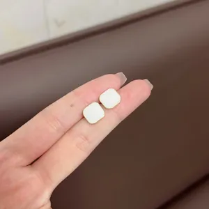 Close-up view of minimalist white square stud earrings with gold edges on fingers.