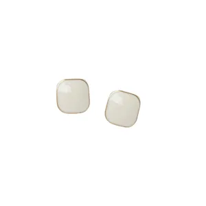 Close-up detail of minimalist square stud earrings in cream white with gold metal frame.