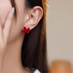 Close-up view of a vibrant red velvet bow stud earring worn on a model's earlobe.