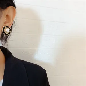 Close-up of elegant Chanel-style round pearl stud earring with gold chain border