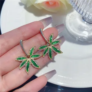 Detailed macro shot of elegant green enamel leaf earrings with pavé rhinestones on hand
