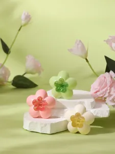 Close-up of flower-shaped air freshener cases in pink, green, and white on stone.
