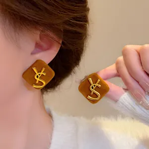 Macro detail of brown velvet square stud earrings featuring a gold metal YSL monogram logo