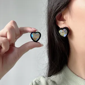 Detailed view of iridescent heart-shaped earrings featuring black velvet trim and gold logos.