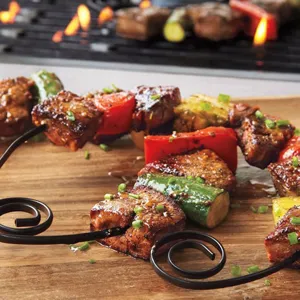 Nahaufnahme von runden schwarzen Antihaft-Grillspießen mit Fleisch und gegrilltem Gemüse