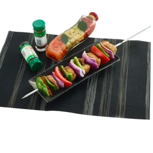 Professioneller Grillspieß aus Edelstahl mit Fleisch und Gemüse auf einem dunklen Platzset