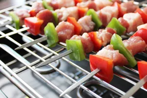 Nahaufnahme von Edelstahl-Grillspießen mit Fleisch und Paprika auf einem Grillrost.