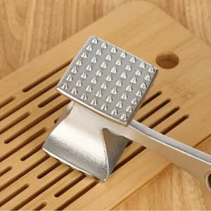 Professioneller doppelseitiger Fleischklopfer aus Metall auf einem hölzernen Schneidebrett