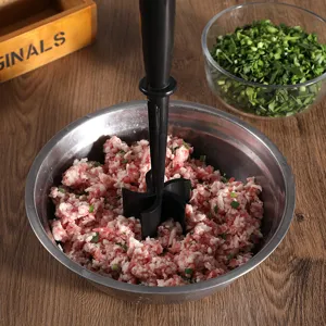 Handheld meat chopper detail mixing minced meat in a steel bowl on a wooden table.