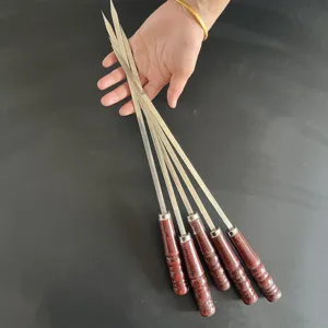 Detailaufnahme von Edelstahl-Grillspießen mit Holzgriffen in der Hand gehalten