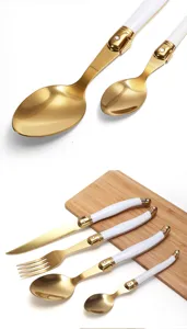 Elegante gouden roestvrijstalen bestekset met witte handvaten op een houten plank