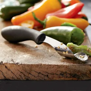 Close-up of stainless steel jalapeño corer tool removing seeds from a green pepper.