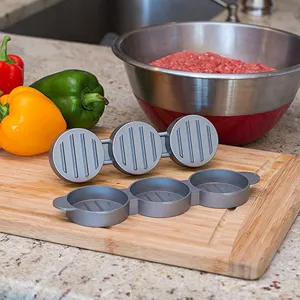 Detail view of a 3-hole circular burger patty press on a wooden board in a kitchen.