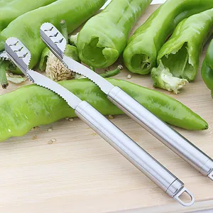 Close-up of stainless steel pepper corer tools on a wooden board with green chilies